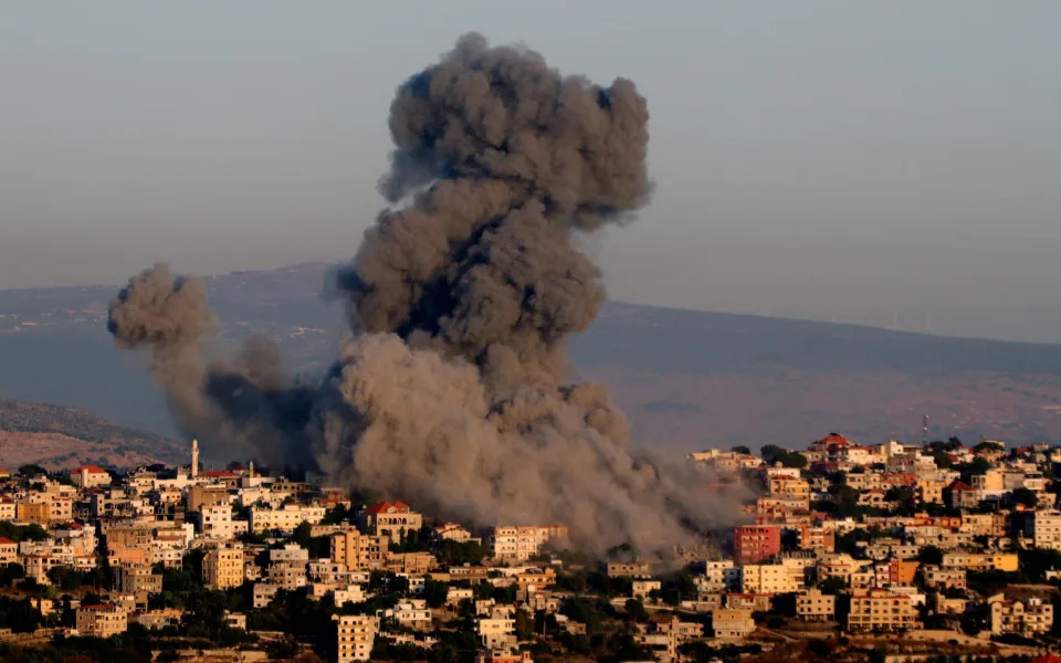 A huge mushroom cloud of black smoke above a hilltop village