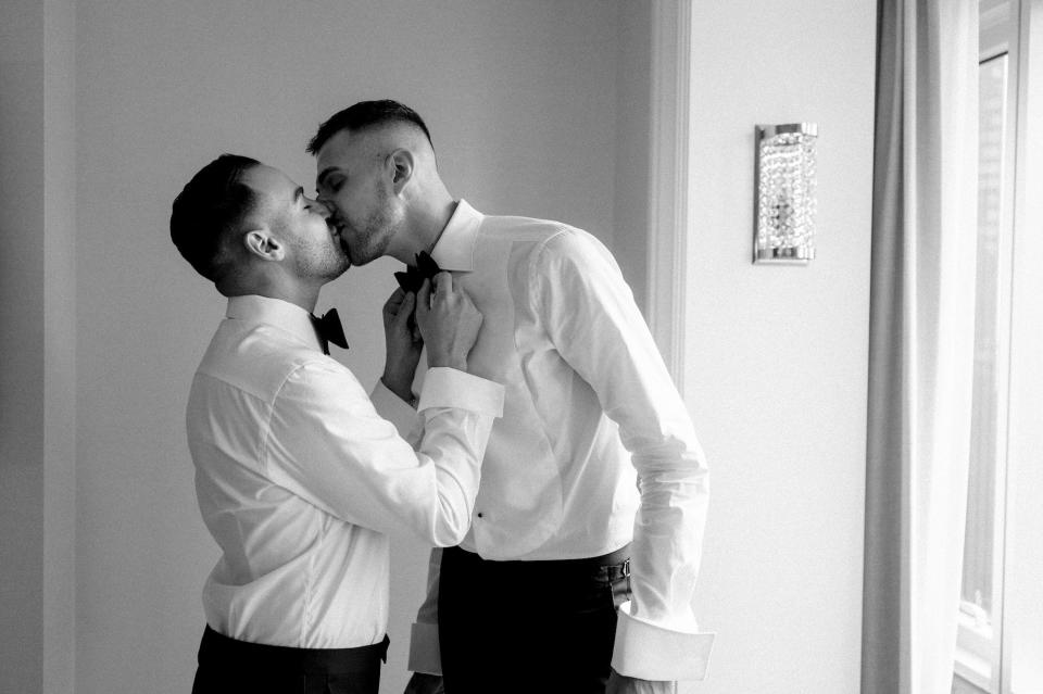 Two grooms kiss as they get ready for their wedding in a black and white photo.