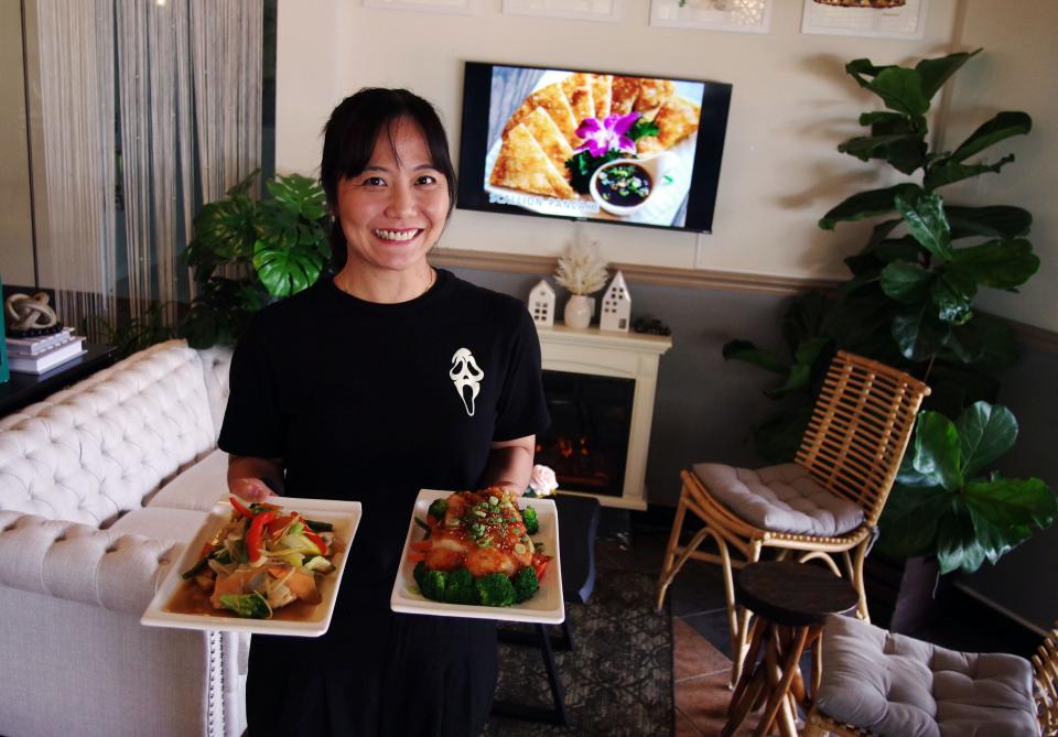 Thai Food Theory restaurant co-owner Jarunee Chansyna stands with two of her best entrees, Salmon Ginger Fish and Orange Chicken on Wednesday, Oct. 25, 2023.