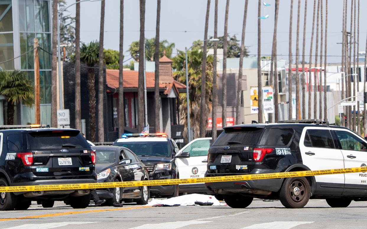 <p>A body covered in a white sheet lies next to a black vehicle covered with stickers and a shattered driver side window, as police cars block traffic at the corner of Fairfax Avenue and Sunset Boulevard in Los Angeles on April 24, 2021 in what appears to be an officer-involved shooting.</p> (AFP via Getty Images)