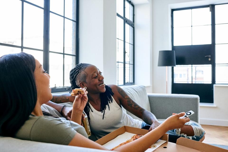 two woman watching movie on couch eating pizza