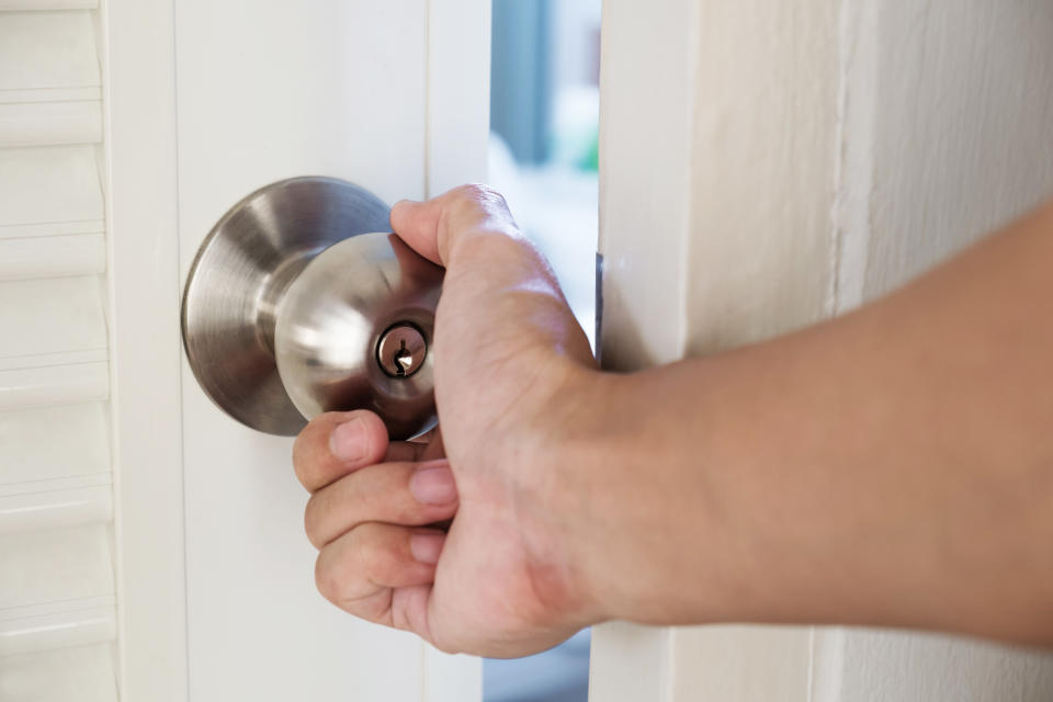 Close-up hand holding door knob, opening door slightly, selective focus