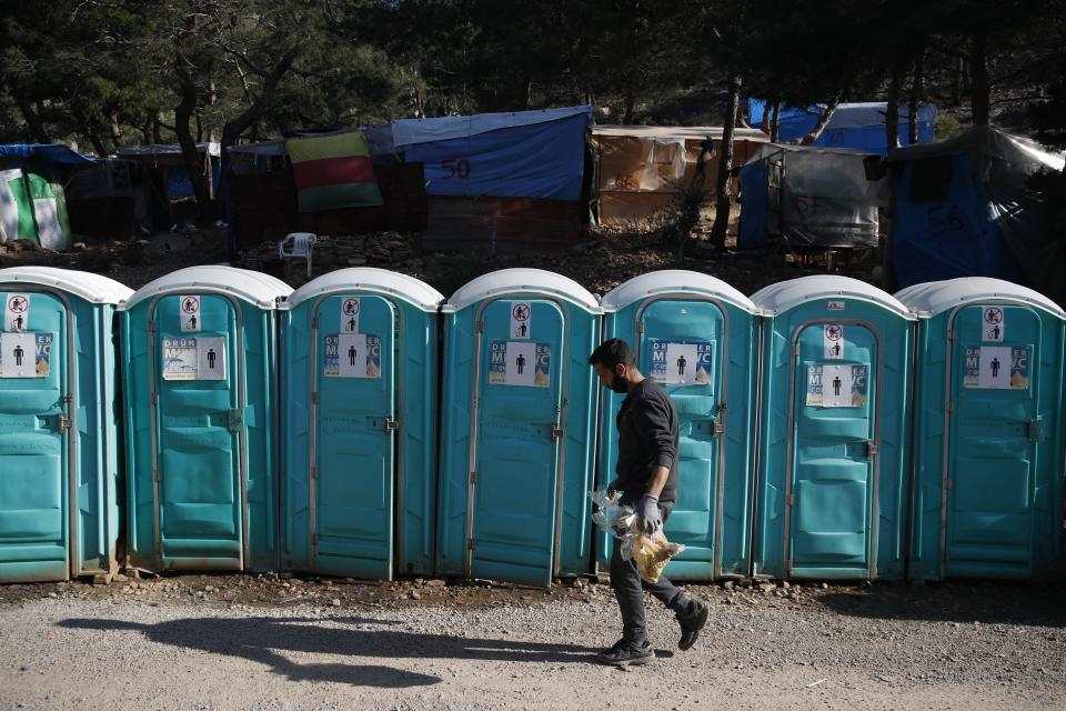 A migrant walks in front of chemical toilets outside the perimeter of the overcrowded refugee camp at the port of Vathy on the eastern Aegean island of Samos, Greece, Wednesday, Feb. 24, 2021. On a hill above a small island village, the sparkling blue of the Aegean just visible through the pine trees, lies a boy’s grave. His first ever boat ride was to be his last - the sea claimed him before his sixth birthday. His 25-year-old father, like so many before him, had hoped for a better life in Europe, far from the violence of his native Afghanistan. But his dreams were dashed on the rocks of Samos, a picturesque Greek island almost touching the Turkish coast. Still devastated from losing his only child, the father has now found himself charged with a felony count of child endangerment. (AP Photo/Thanassis Stavrakis)