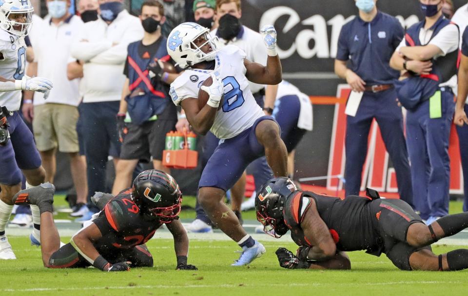 Miami linebacker Zach McCloud (53) and cornerback Isaiah Dunson (29) stop North Carolina running back Michael Carter (8) during the first half of an during an NCAA college football game at Hard Rock Stadium In Miami Gardens, Fla, Saturday, Dec, 12, 2020. (Al Diaz/Miami Herald via AP)