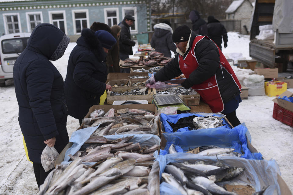 In this photo taken on Saturday, Dec. 1, 2018, a woman sells smoked fish at Saturday's market in Milove town at the border between Ukraine and Russia, Luhansk region, eastern Ukraine . On the map, Chertkovo and Melove is one village, crossed by railroad tracks and a main road called the Friendship of Peoples Street. That slogan still rings true for many locals, but is being sorely tested by the animosity between their two nations, Russia and Ukraine. (AP Photo/Evgeniy Maloletka)