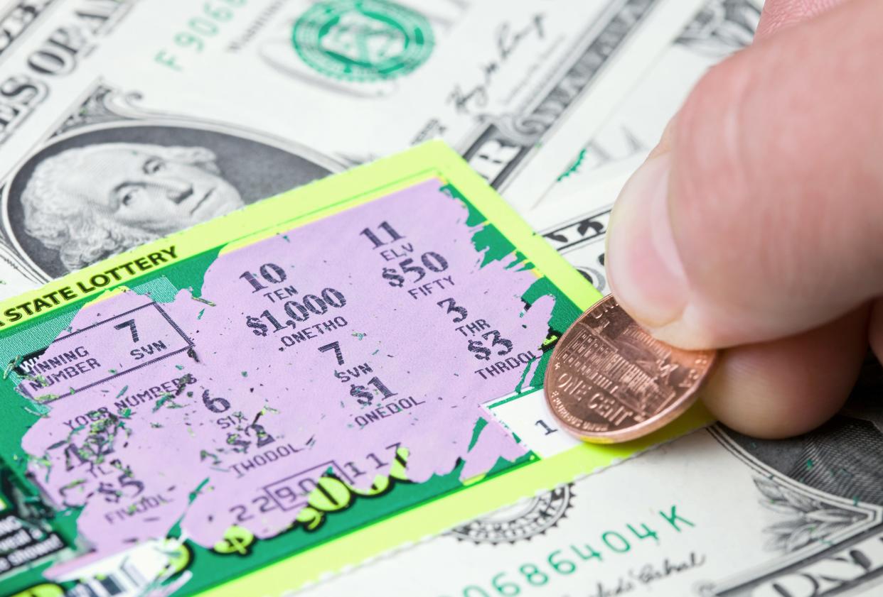 A lottery player scratching a winning ticket which rests on a dollar bill background.