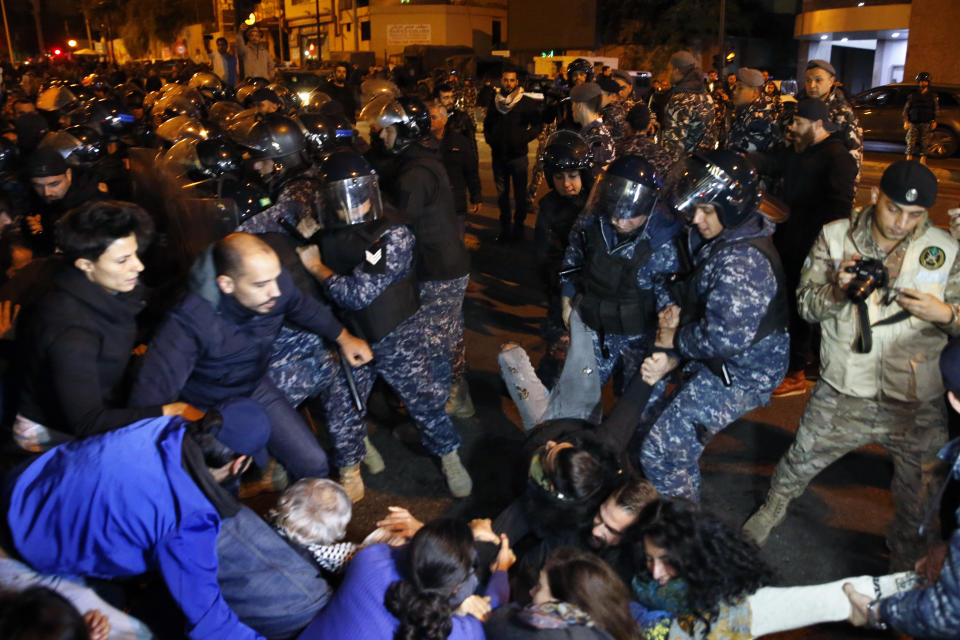 Protesters lie on a road, as they scream and hold each others while riot police try to remove them and open the road, in Beirut, Lebanon, Wednesday, Dec. 4, 2019. Protesters have been holding demonstrations since Oct. 17 demanding an end to widespread corruption and mismanagement by the political class that has ruled the country for three decades. (AP Photo/Bilal Hussein)