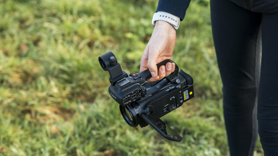 The Canon XA65 camcorder being held above grass by a female hand