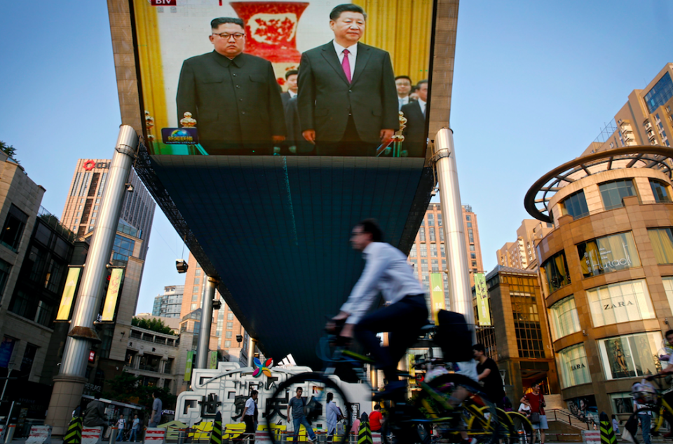 <em>People bicycle past a giant TV screen broadcasting the meeting in Beijing (AP)</em>