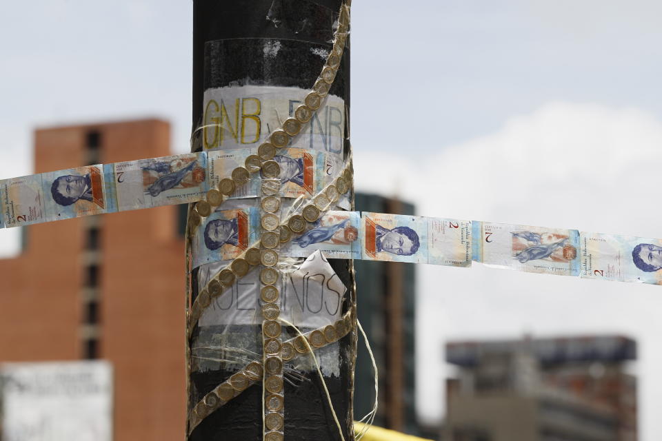 FILE - In this July 20, 2017 file photo, devalued Bolivar bank notes and coins, taped together, serve as makeshift rope at a roadblock set up by anti-government protesters in Caracas, Venezuela. Forced to meet interest payments on the few remaining loans and bonds the government hasn’t yet defaulted on, the government must finance its huge budget deficit by printing even more bolivars, further accelerating prices. (AP Photo/Ariana Cubillos, File)