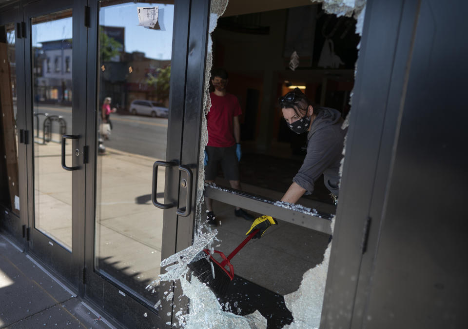 Megan Culverhouse, an employee at John Fluevog shoe store, cleans up broken glass from a window of the Uptown Theatre after both businesses were hit by gunfire from an early morning shooting Sunday, June 21, 2020, in Minneapolis' Uptown neighborhood. (Jerry Holt/Star Tribune via AP)