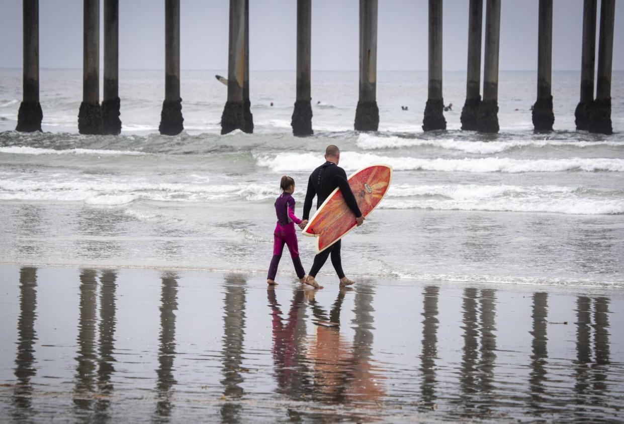 Beachgoers hold hands while heading out to surf at low tide on the last day of open beaches in
