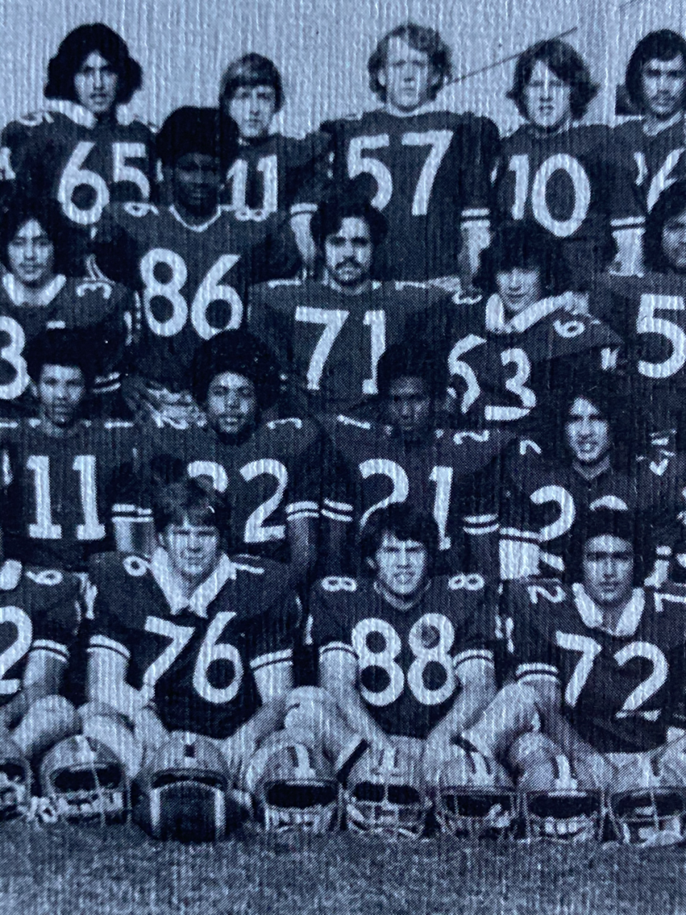 High school football players in uniform stand in rows.
