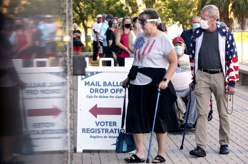 Voters Jenny Hart, center, and James Hart, of Clearwater, wait in line to enter the Supervisor of Elections Office at the Pinellas County Courthouse, during early voting on Monday, Oct. 19, 2020, in Clearwater, Fla. (Douglas R. Clifford/Tampa Bay Times via AP)
