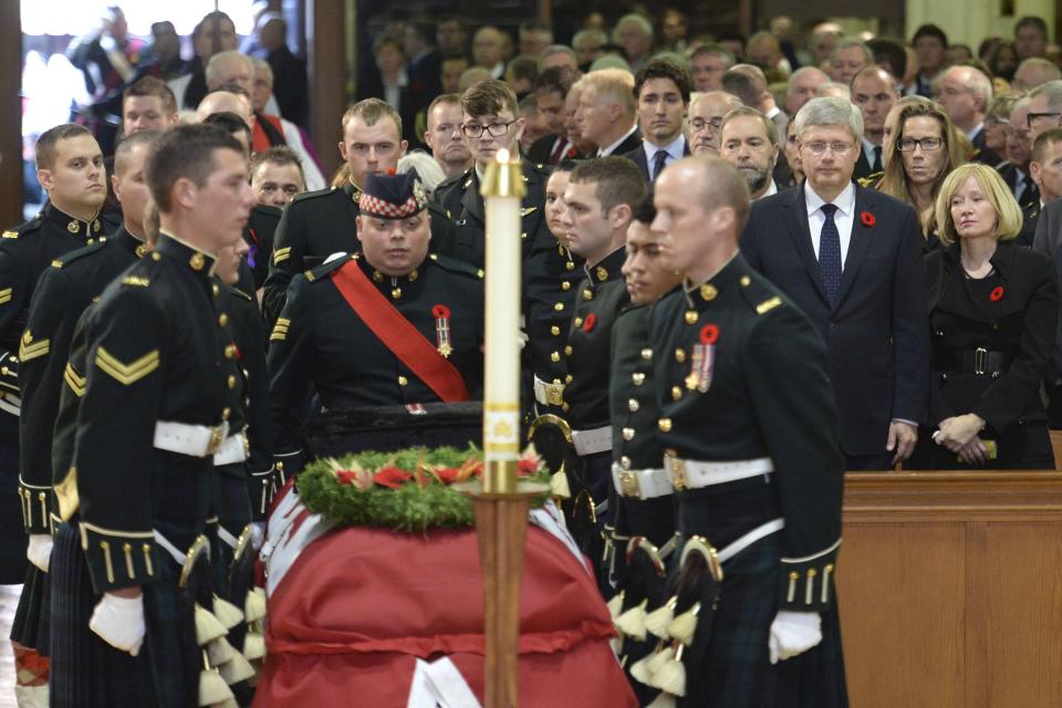 Canadian Prime Minister Stephen Harper and his wife Laureen (R) rise as the coffin of Cpl. Nathan Cirillo is carried by pallbearers at his regimental funeral service in Hamilton, Ontario October 28, 2014. Cirillo was standing guard at the National War Memorial in Ottawa last Wednesday when he was killed by a gunman who went on to open fire on Parliament Hill. REUTERS/Nathan Denette/Pool (CANADA - Tags: POLITICS MILITARY CRIME LAW OBITUARY)