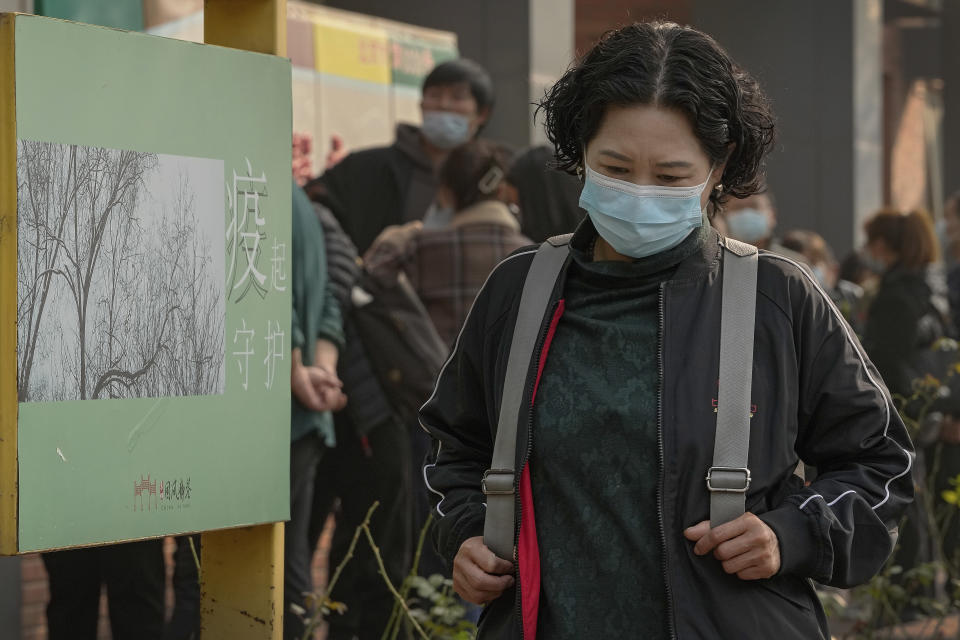 A woman wearing a face mask to help curb the spread of the coronavirus walks by a poster baring the words: "Epidemic protection" as masked residents line up to receive booster shots against COVID-19 at a vaccination site in Beijing, Monday, Oct. 25, 2021. A northwestern Chinese province heavily dependent on tourism closed all tourist sites Monday after finding new COVID-19 cases. (AP Photo/Andy Wong)