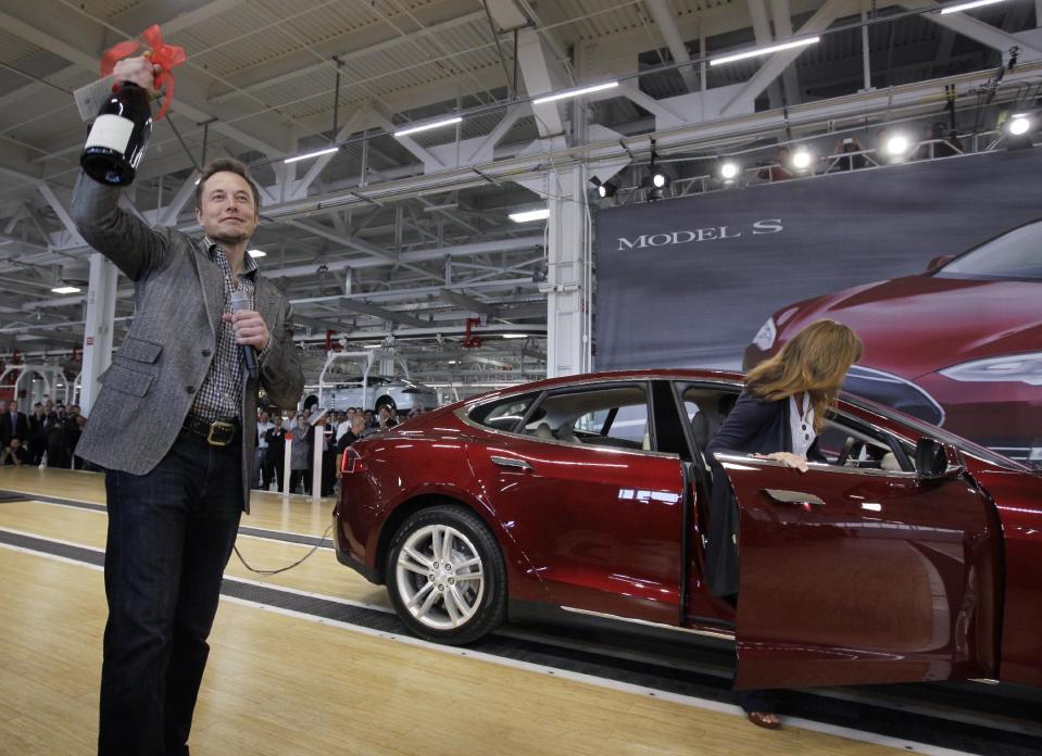 FILE - In this June 22, 2012 file photo, Tesla Motors Inc. CEO Elon Musk holds up a bottle of wine given as a gift from one of their first customers, right, during a rally at the Tesla factory in Fremont, Calif. When billionaire entrepreneur Elon Musk published fanciful plans to shoot capsules full of people at the speed of sound through a tube connecting Los Angeles and San Francisco, he asked the public to perfect his rough plans. From tinkerers to engineers, the race is on. (AP Photo/Paul Sakuma, File)