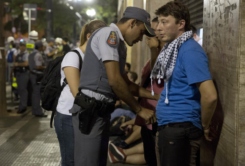 Photojournalist Victor Moriyama is frisked by a policeman after being detained while covering a protest against the upcoming World Cup soccer tournament in Sao Paulo, Brazil, Saturday, Feb. 22, 2014. Hundreds of protesters gathered demonstrating against the billions of dollars being spent to host this year's World Cup while the nation's public services remain in a woeful state. The protest started peacefully, but adherents to the Black Block anarchist tactics vandalized banks and clashed with police, who used tear gas and stun grenades to disperse the violent demonstrators. Local journalists also complained of police knocking cameras from their hands and roughing them up. (AP Photo/Andre Penner)