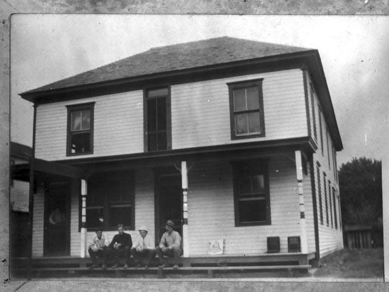 This is a photograph showing the hotel in Clements, Kansas. Two of the people sitting on the porch are identified as H. B. Jackson (far right) and Edwin Jackson (second from the left wearing a dark shirt). Taken between 1909 and 1910.