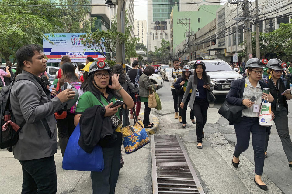 Office employees, some wearing hard hats, file out of their building following a magnitude 5.5 that rocked some areas of the country's north, including in the capital, that also briefly disrupted train services Friday, Sept. 13, 2019 in Manila, Philippines. The Philippine Institute of Seismology and Volcanology says Friday's quake was centered about 40 kilometers northeast of the coastal town of Burdeos in northeastern Quezon province and was caused by movement in a local fault at a shallow depth of 10 kilometers (6 miles). There were no immediate reports of injuries or damages. (AP Photo/Bullit Marquez)