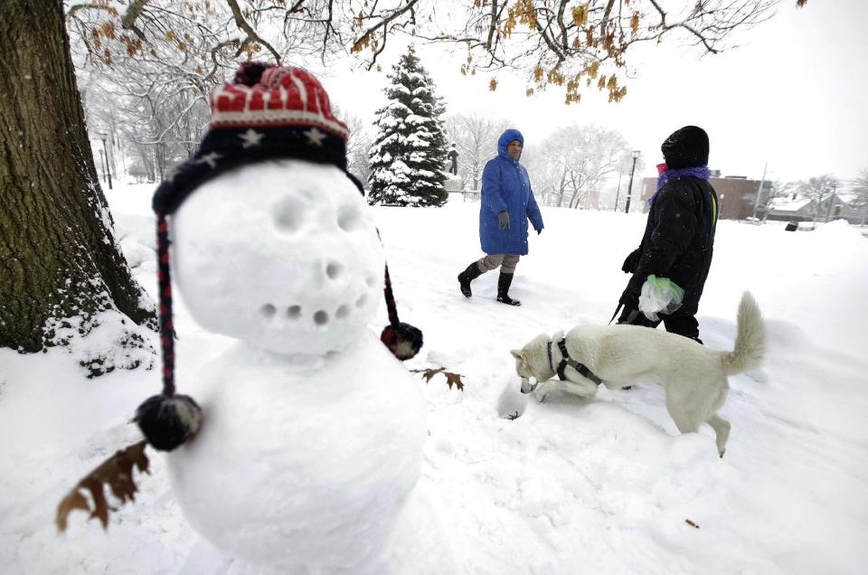 Tina Fuller, 60, of Waltham, Mass., behind center, walks past a snowman and a person walking a dog, Sunday, Feb. 12, 2017, in Waltham, Mass. Officials in the Northeast are urging people take precautions and schools have begun announcing cancellations as another winter blast of snow moved into the region. (AP Photo/Steven Senne)