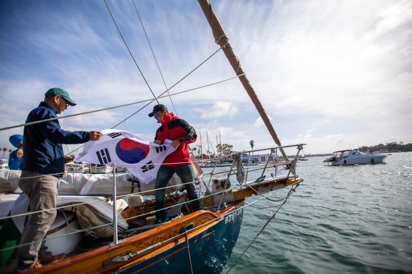 Marina Del Rey, CA - March 04: Captain Jin Woo Nam, left, and Joseph Chang, right, carry a Korean flag on the 37-foot, 32,000-pound Tayana sailing yacht named "Ignatella," on Saturday, March 4, 2023, in Marina Del Rey, CA. Today the men are setting sail for a three-month-long sailboat journey across the Pacific Ocean, from Marina del Rey to Honolulu and ultimately to Incheon, South Korea.(Francine Orr / Los Angeles Times)