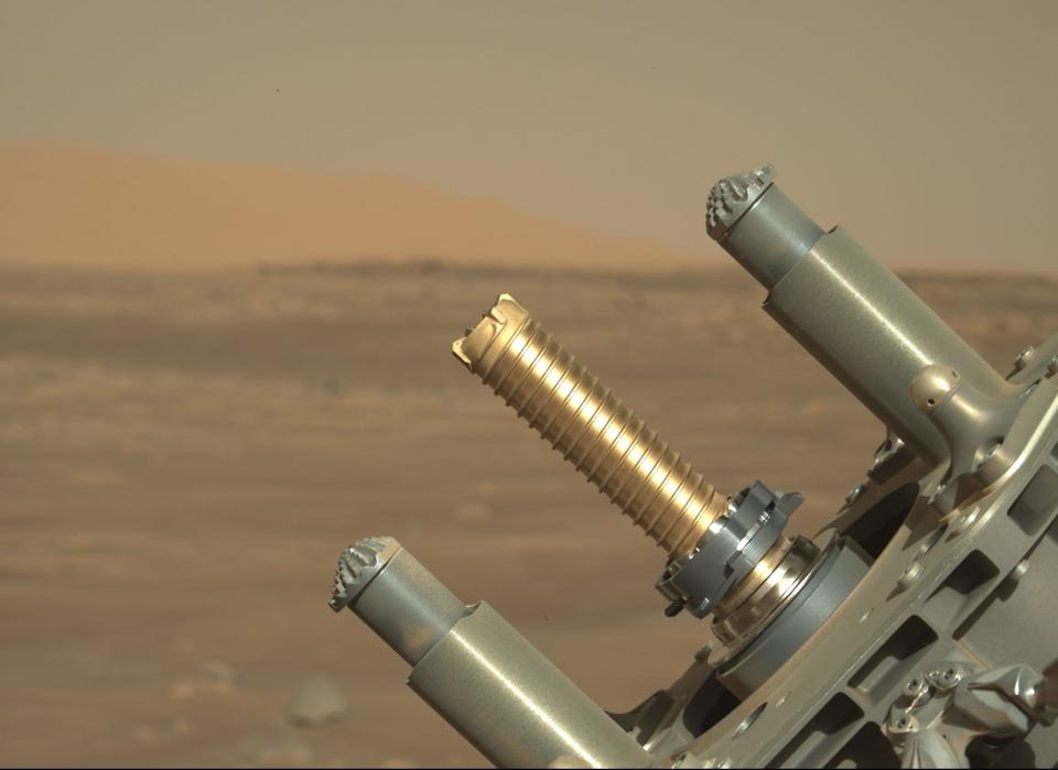 perseverance rover robotic arm holds up golden tube for coring samples against mars plains background