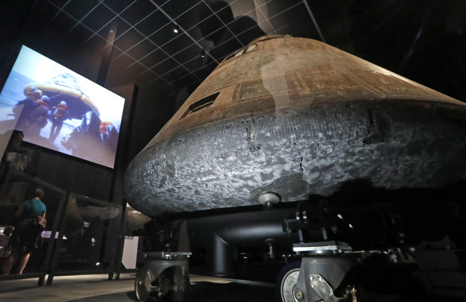 As historic videos of the craft are shown in the background, the NASA Apollo 11 command module Columbia, its bottom scorched and pitted from reentry into Earth's atmosphere decades earlier, is displayed at the centerpiece of an Apollo 11 mission exhibit at the Museum of Flight, Friday, July 19, 2019, in Seattle. The exhibit commemorates the historic landing by American astronauts on the moon 50 years earlier, on July 20, 1969. (AP Photo/Elaine Thompson)