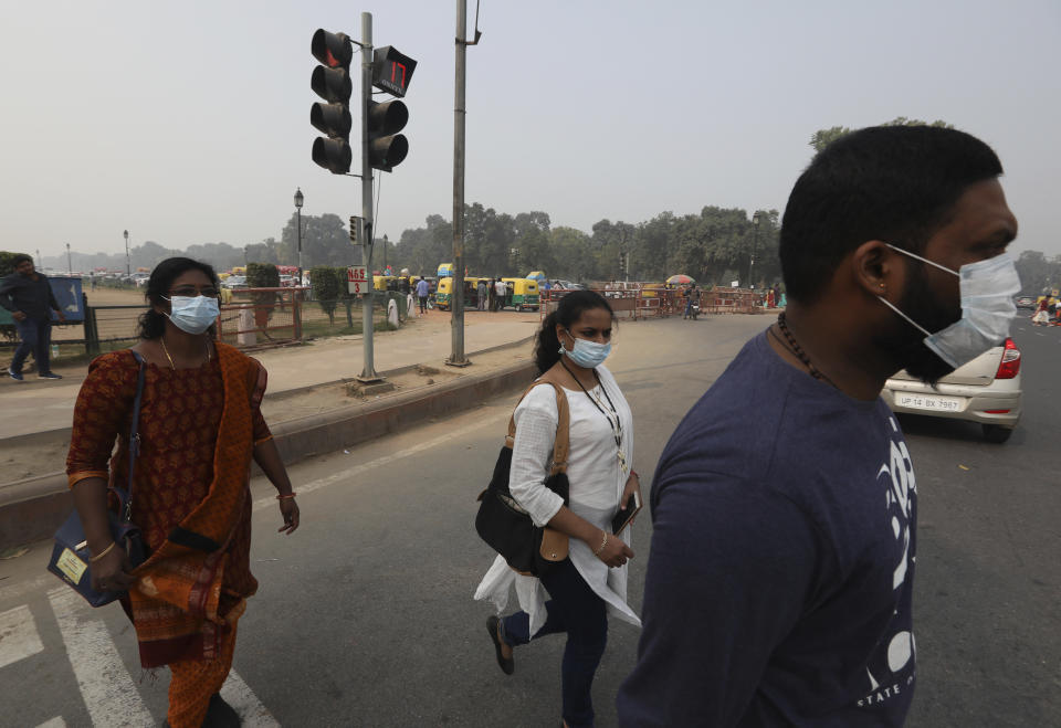 Tourists wear mask to save themselves from pollution as they cross a road amidst thick layer of smog in New Delhi, India, Tuesday, Nov. 12, 2019. A thick haze of polluted air is hanging over India's capital, with authorities trying to tackle the problem by sprinkling water to settle dust and banning some construction. The air quality index exceeded 400, about eight times the recommended maximum. (AP Photo/Manish Swarup)