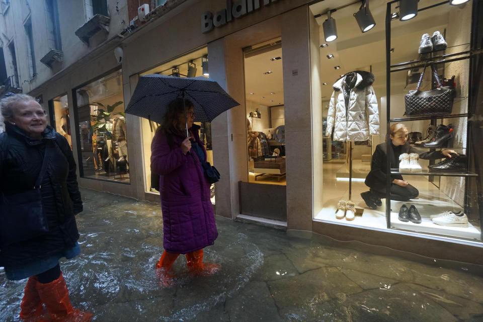 A shop assistant adjusts shoes as women outside wade through a flooded street on the occasion of a high tide, in Venice, Italy, Tuesday, Nov. 12, 2019. (Photo: Andrea Merola/ANSA via AP)