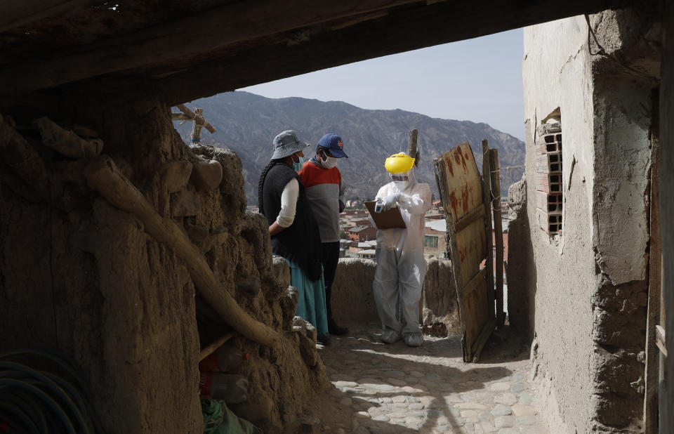 Vestidos en trajes de protección, doctores hablan con residentes durante una campaña de testeo de coronavirus casa por casa en Avircato, Bolivia, el martes 7 de julio de 2020. (AP Foto/Juan Karita)