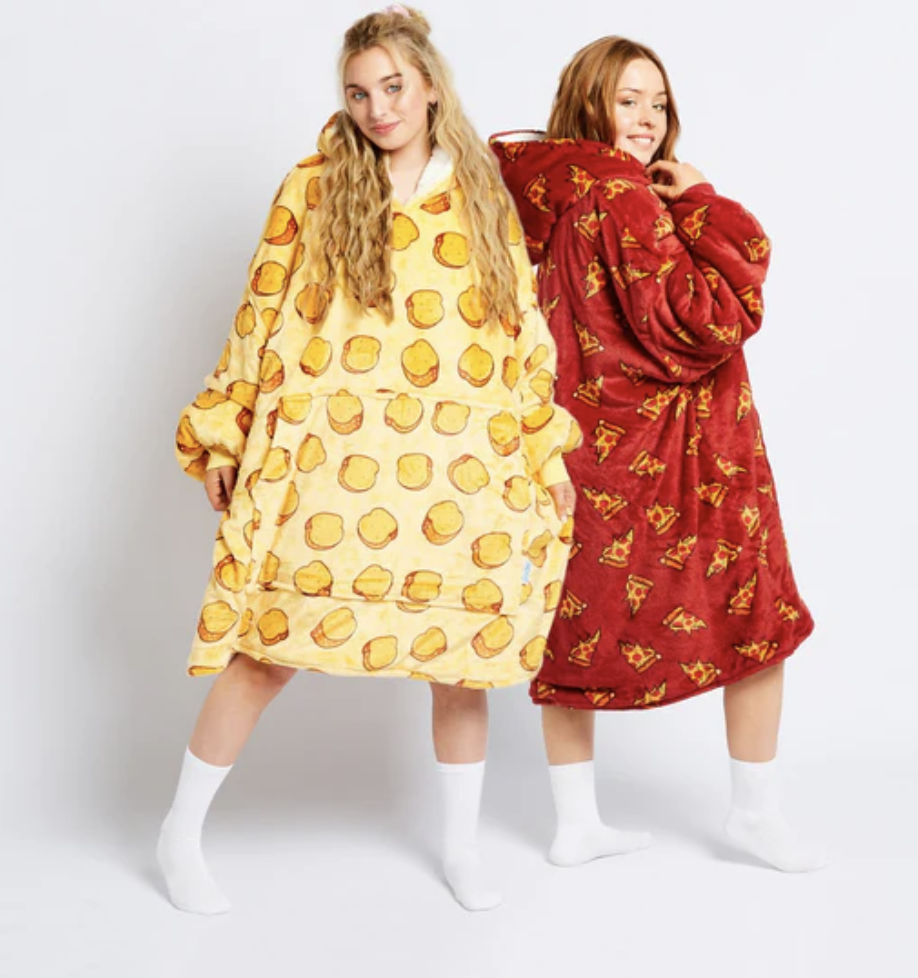 Two women stand side by side in Oodies, one yellow Oodie with loaf of bread print and one red Oodie with pizza print