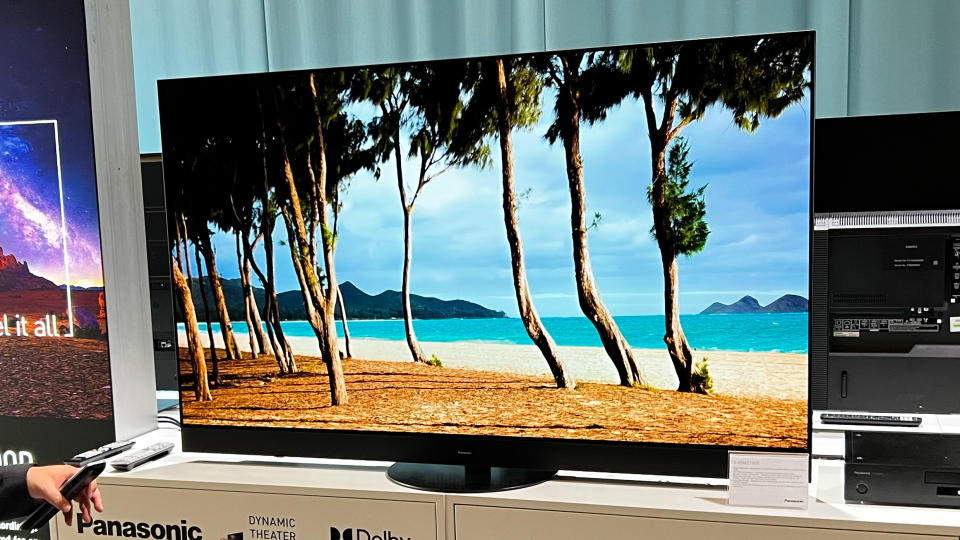 Panasonic LZ1500 TV shows an image of palm trees on a beach. The TV is standing on a shelf at a trade show