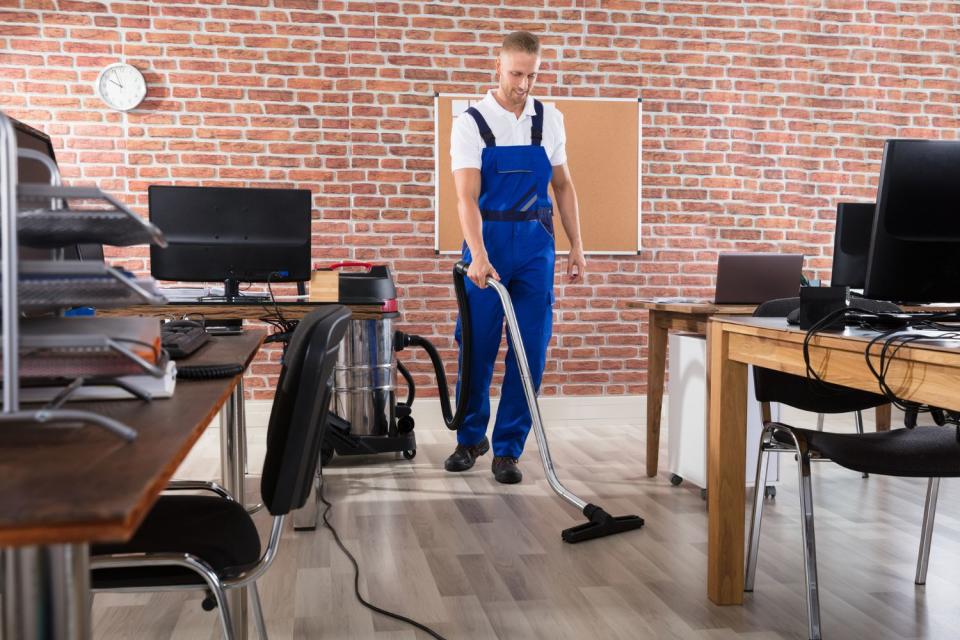 A man cleans a floor with a vacuum cleaner.