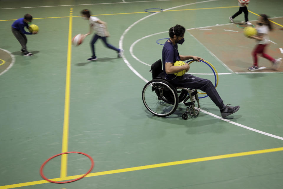 Adolfo Damian Berdun, of Argentina, a professional player and captain of the Argentine basketball Paralympic team, teaches children basketball at a primary school in Verano Brianza, outskirt of Milan, Italy, Tuesday, May 11, 2021. Four second-grade classes in the Milan suburb of Verano Brianza have been learning to play basketball this spring from a real pro. They also getting a lesson in diversity. Their basketball coach for the last month has been Adolfo Damian Berdun, an Argentinian-Italian wheelchair basketball champion. Berdun, 39, lost his left leg in a traffic accident at ag 13 in his native Buenos Aires, and he has visited many schools over the years to discuss how he has lived with his disability. (AP Photo/Luca Bruno)