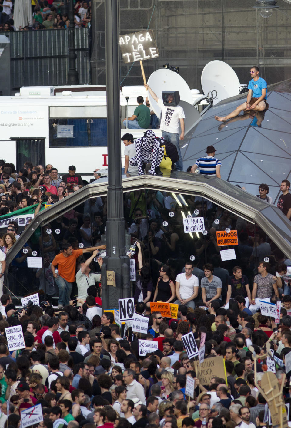 A protester standing on the subway dome entrance holds a sign saying "switch off the TV" in Puerta del Sol plaza in central Madrid, Saturday May 12, 2012. Protesters returned to Sol to mark the anniversary of the protest movement that inspired groups in other countries. The protests began May 15 last year and drew hundreds and thousands of people calling themselves the indignant movement. The demonstrations spread across Spain and Europe as anti-austerity sentiment grew. (AP Photo/Paul White)