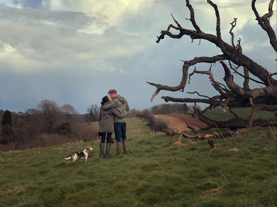 Meghan Markle and Prince Harry kiss with their back to the camera. They are walking with a dog in the British countryside. (Netflix)