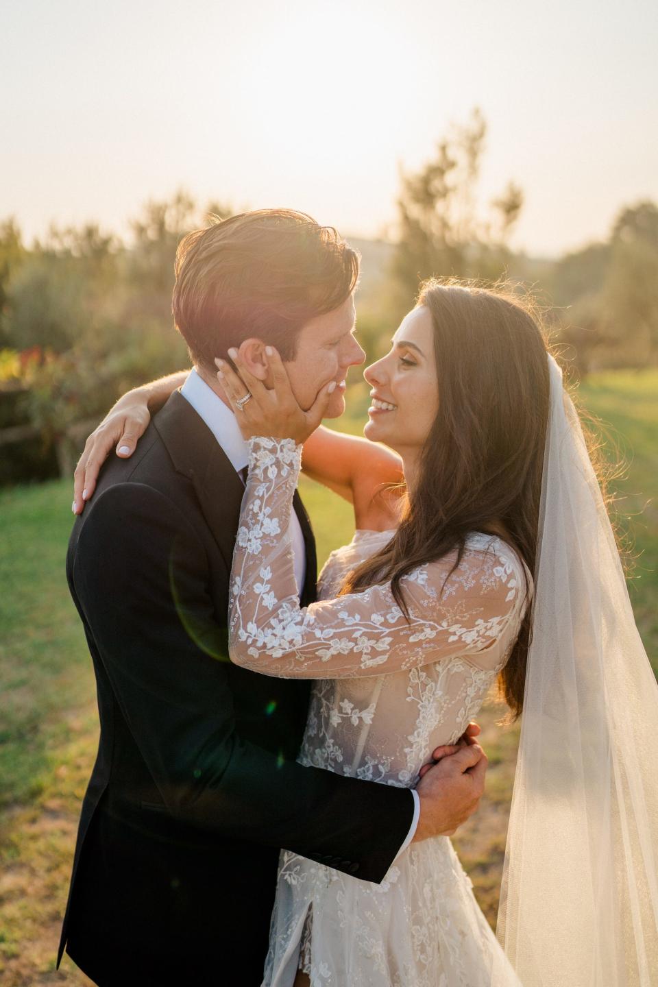 A bride grabs her groom's face as they hug and smile at each other.