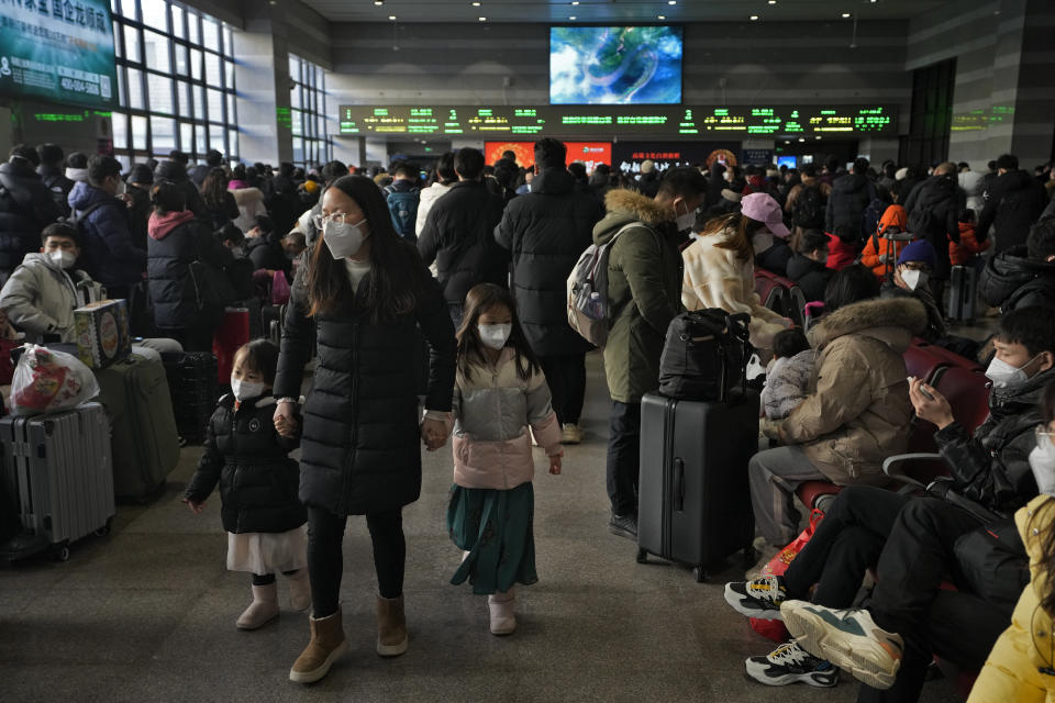 A woman and children wearing face masks walk by masked travelers wait at a departure hall to catch their trains at the West Railway Station in Beijing, Sunday, Jan. 15, 2023. The World Health Organization has appealed to China to keep releasing information about its wave of COVID-19 infections after the government announced nearly 60,000 deaths since early December following weeks of complaints it was failing to tell the world what was happening. (AP Photo/Andy Wong)