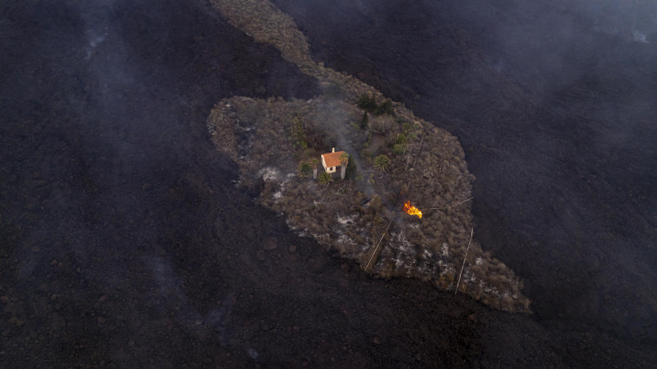 In this photo provided by iLoveTheWorld, a house remains intact as lava flows after a volcano erupted near Las Manchas on the island of La Palma in the Canaries, Spain, Monday, Sept. 20, 2021. A dormant volcano on a small Spanish island in the Atlantic Ocean erupted on Sunday, forcing the evacuation of thousands of people. Huge plumes of black-and-white smoke shot out from a volcanic ridge where scientists had been monitoring the accumulation of molten lava below the surface. (Alfonso Escalero/iLoveTheWorld via AP)