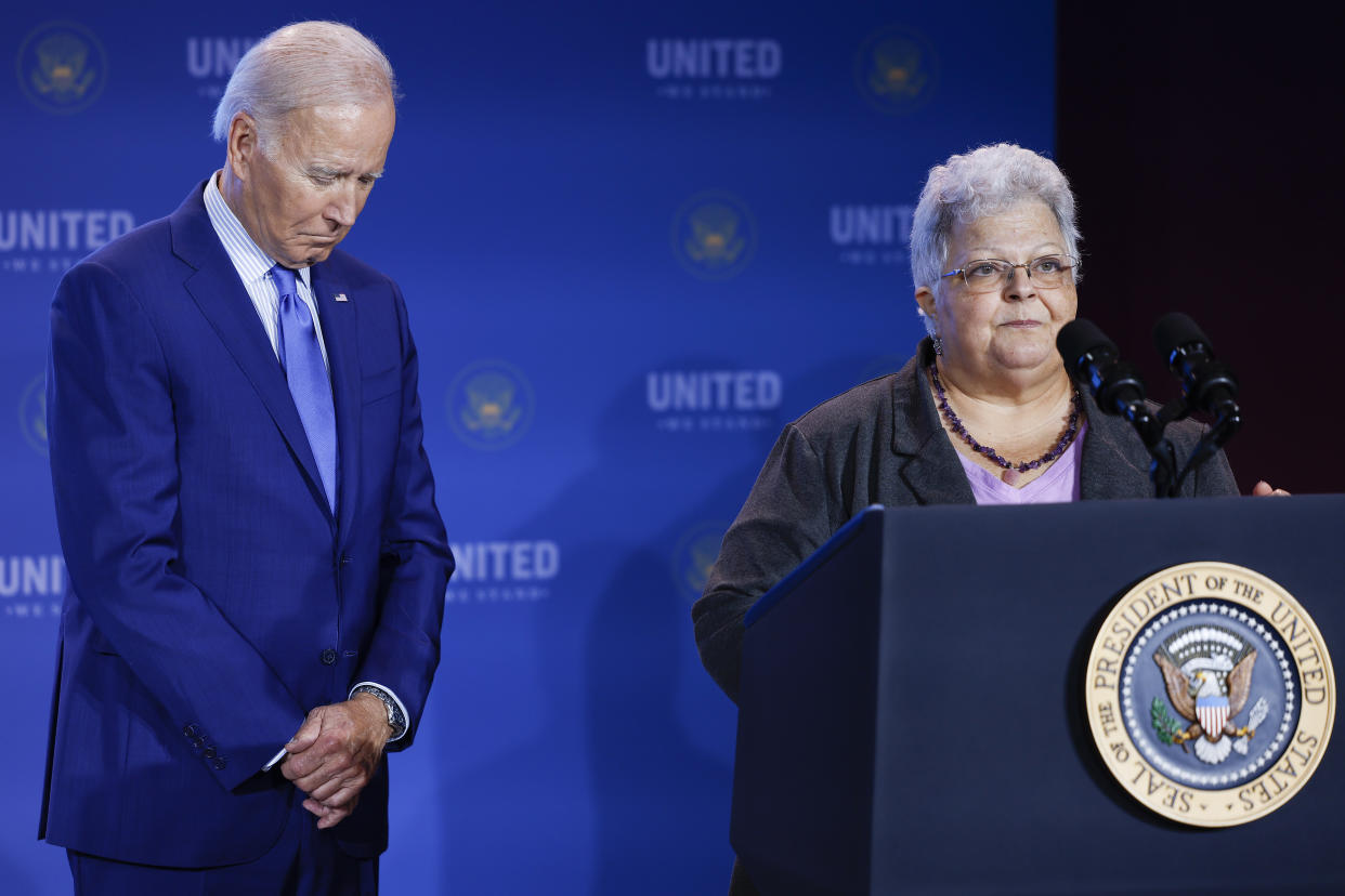President Biden looks down solemnly as Susan Bro delivers remarks from a podium.