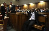 Oscar Pistorius, second from left, speaks to an unidentified member of his legal team as he stands in the dock prior to the start of his trial at the high court in Pretoria, South Africa, Monday, March 3, 2014. Pistorius is charged with murder with premeditation in the shooting death of girlfriend Reeva Steenkamp in the pre-dawn hours of Valentine's Day 2013. (AP Photo/Themba Hadebe, Pool)