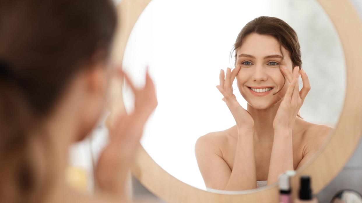 mujer masajeando sus ojos mientras se mira al espejo