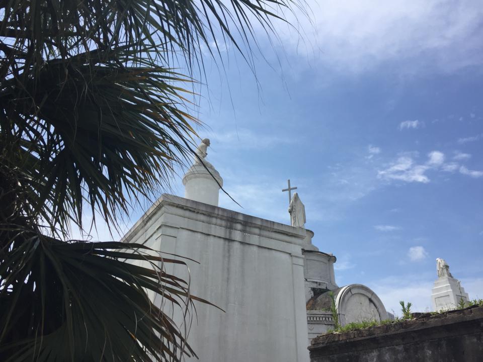 This June 3, 2018 photo in St. Louis Cemetery No. 1 in New Orleans shows its above ground burial vaults pictured against a blue sky. The vaults are laid out like little houses in maze-like aisles that feel like tiny streets. Some tombs are decorated with sculptures and crosses. Many are in a picturesque state of decay, revealing layers of paint, brick and stone while weeds sprout through the cracks. (AP Photo/Beth J. Harpaz)