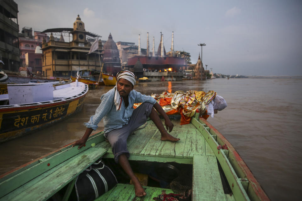 A worker who helps cremate bodies sits by the body of an elderly man, wrapped and weighed down by a large rock, before throwing the body into the river Ganges as per his final wish, on the banks of river Ganges in Varanasi, India, Friday, Oct. 18, 2019. For millions of Hindus, Varanasi is a place of pilgrimage and anyone who dies in the city or is cremated on its ghats is believed to attain salvation and freed from the cycle of birth and death. Tens of thousands of corpses are cremated in the city each year, leaving half-burnt flesh, dead bodies and ash floating in the Ganges. (AP Photo/Altaf Qadri)