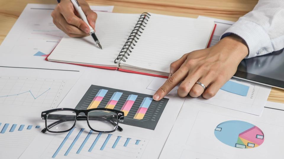 woman writing in noteapd pointing at charts graphs