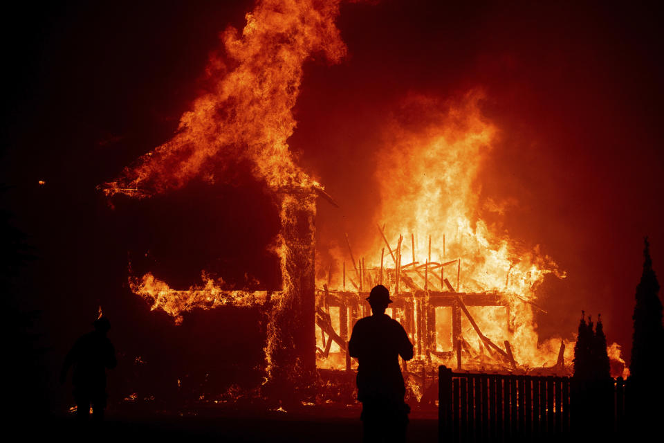 FILE - In this Nov. 8, 2018 file photo, a home burns as a wildfire called the Camp Fire rages through Paradise, Calif. Experts say it’s hard to know what might have happened had the power stayed on, or if the utility’s proactive shutoffs are to thank for California’s mild fire season this year. (AP Photo/Noah Berger, File)