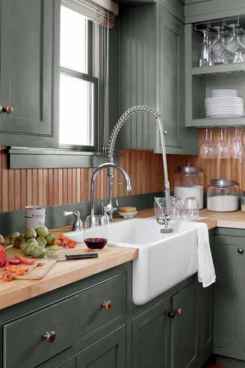 a corner of a kitchen that has green cabinets and wood countertops and a wood backsplash too