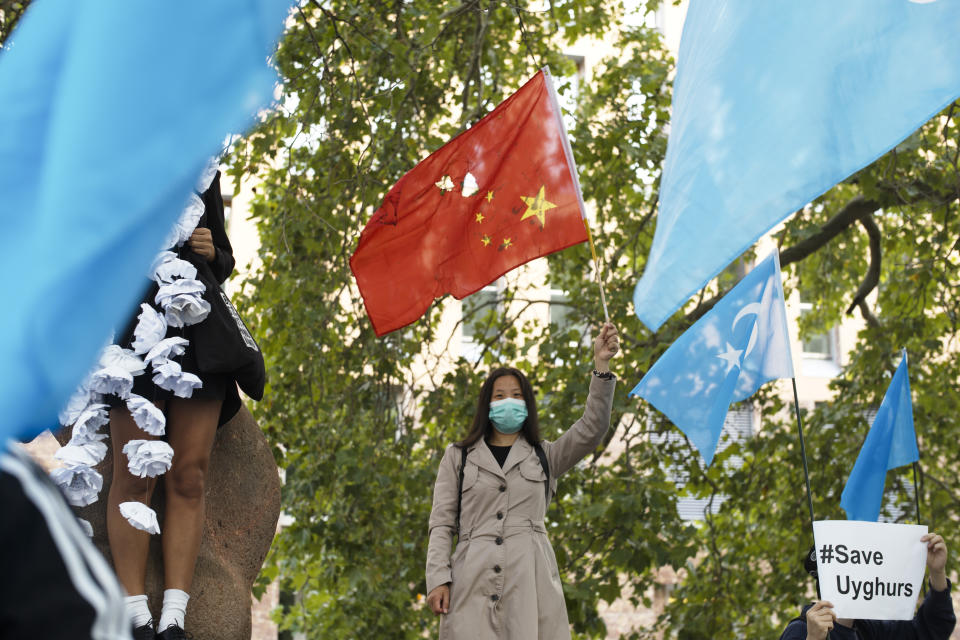 A woman with a partly destroyed Chinese flag stand between demonstrators with Uyghur flags as she attends a protest during the visit of Chinese Foreign Minister Wang Yi in Berlin, Germany, Tuesday, Sept. 1, 2020. German Foreign Minister Heiko Maas meets his Chinese counterpart at the foreign ministry guest house Villa Borsig for bilateral talks. (AP Photo/Markus Schreiber)