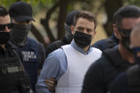 Helicopter pilot Babis Anagnostopoulos, center, escorted by police officers arrives to the prosecutor's office at a court to give evidence, in Athens, Tuesday, June 22, 2021. Anagnostopoulos was charged last Friday with the murder of his British-Greek wife, Caroline Crouch, 20, whose death he had initially claimed was caused by burglars during a brutal invasion of their home on the outskirts of Athens. (AP Photo/Petros Giannakouris)